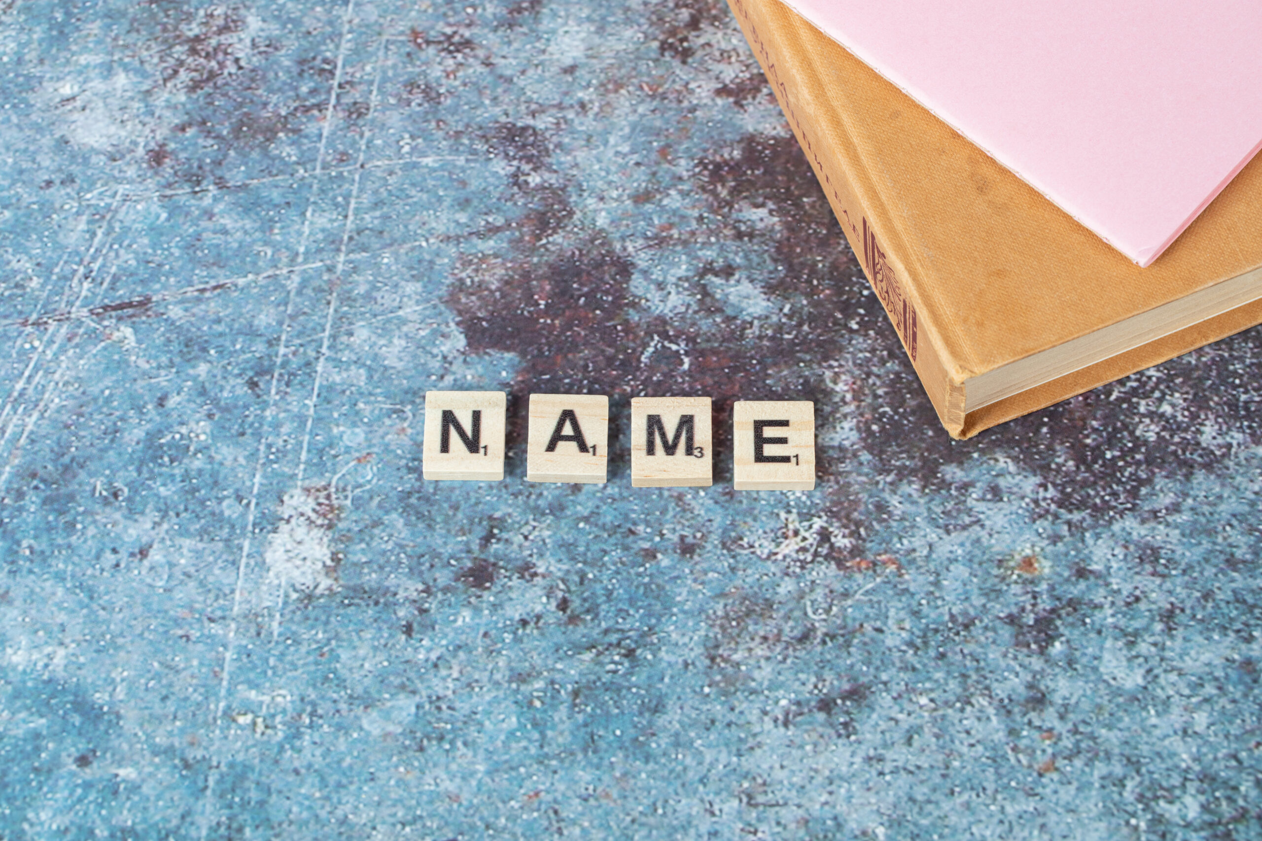 Name writing with black letters on wooden dices with an old book around. High quality photo